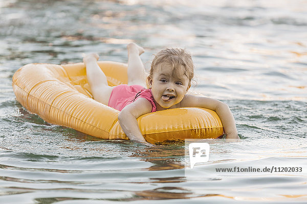 Cheerful cute girl floating on raft in lake