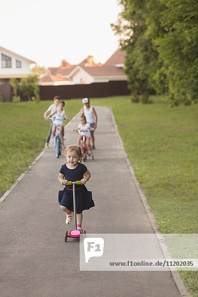 Mädchenradfahren mit Geschwistern auf der Straße inmitten eines grasbewachsenen Feldes im Park
