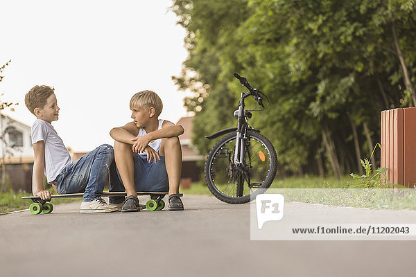 Friends talking while sitting on skateboard by bicycle at park