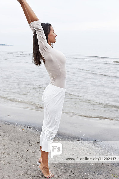 Young woman stretching on beach by sea