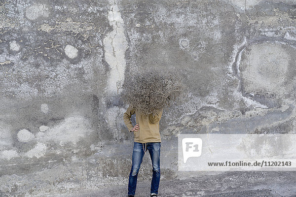 Mann hält trockenen Busch  während er an einer verwitterten Wand steht.