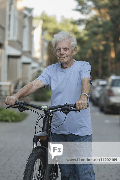 Portrait of senior adult standing with bicycle on city street