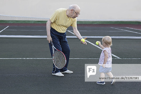 Mädchen gibt Großvater Tennisball,  während sie auf dem Spielfeld steht.