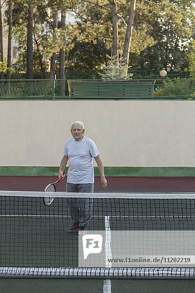 Senior man playing tennis against wall at playing field