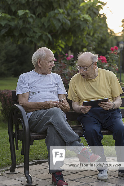 Seniorenfreunde beim Sitzen auf der Parkbank mit Technik