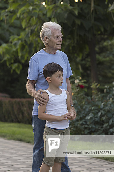 Smiling grandfather standing with grandson on footpath at park