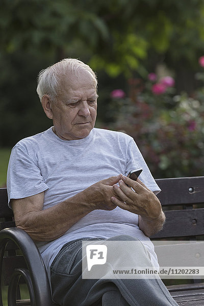 Smiling man using smart phone while sitting on park bench