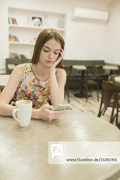Junge Frau beim Kaffeetrinken im Café am Telefon