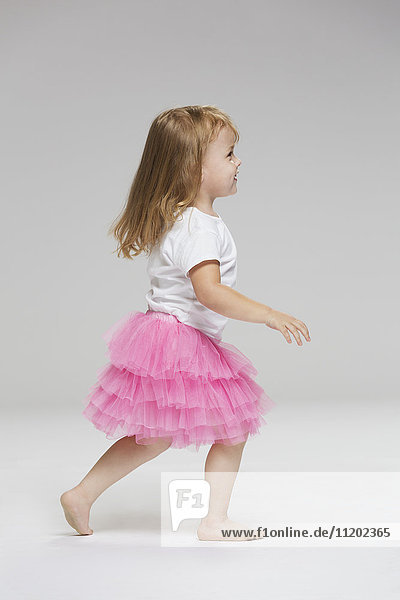 Side view of girl wearing tutu playing against gray background