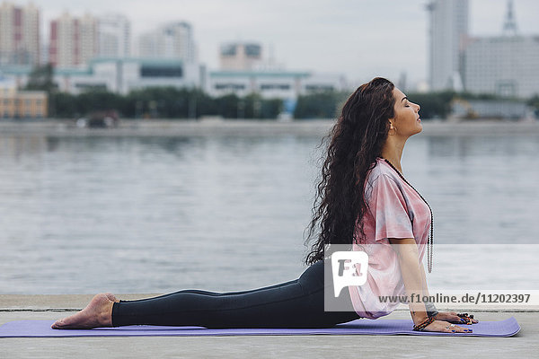 Seitenansicht der Yoga praktizierenden Frau in Cobra-Pose am Fluss in der Stadt