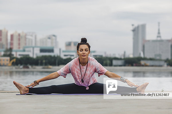 Schöne Frau  die Yoga gegen den Fluss in der Stadt praktiziert.