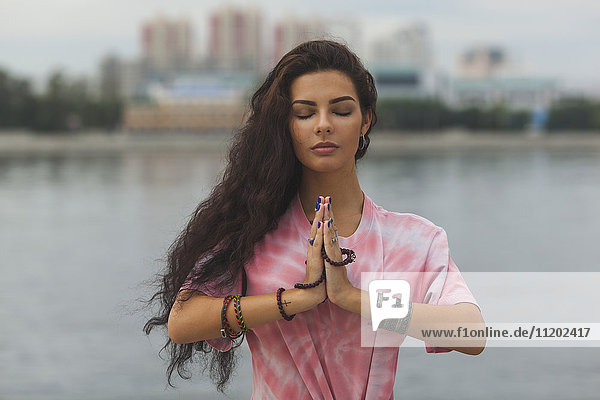 Frau mit geschlossenen Augen meditiert in Gebetsstellung gegen den Fluss