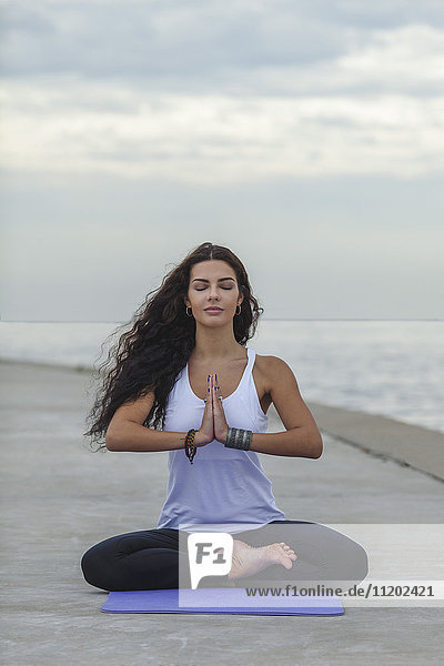 Frau mit geschlossenen Augen praktiziert Yoga in Gebetsposition am Strand gegen den bewölkten Himmel.