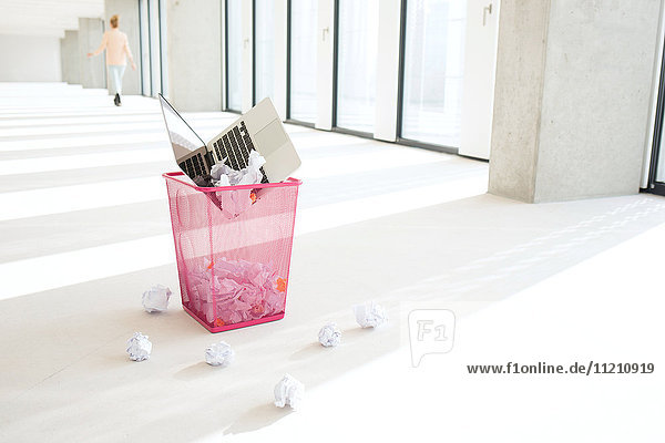 Laptop and crumpled papers in garbage bin at office