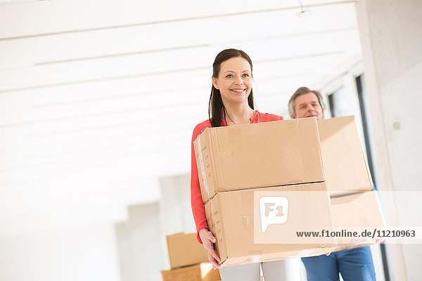 Smiling businesswoman with male colleague carrying cardboard boxes in new office