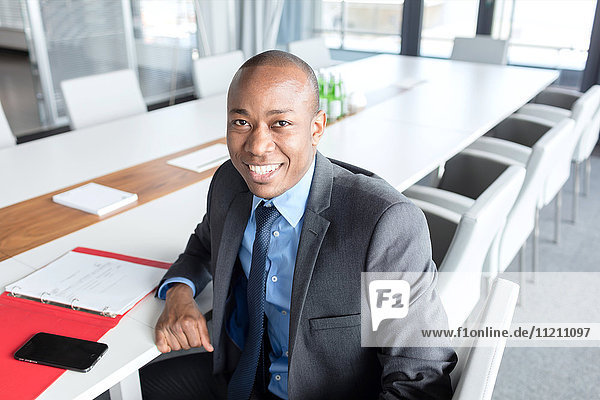 Porträt eines lächelnden jungen Geschäftsmannes  der am Konferenztisch sitzt