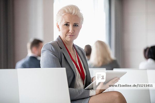 Porträt einer selbstbewussten Geschäftsfrau  die ein digitales Tablet hält  während sie im Seminarraum sitzt