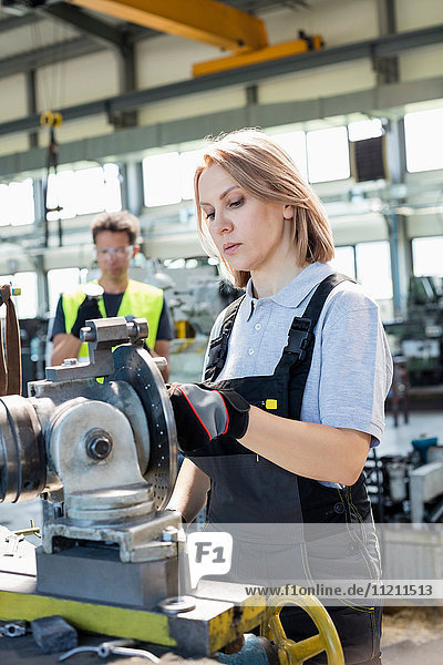 Mature female worker working on machinery with colleague in background at factory