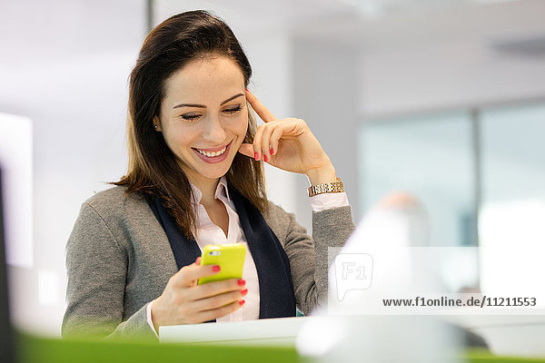Smiling young businesswoman reading text message on smartphone at office