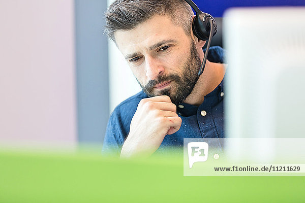 Thoughtful mid adult businessman wearing headset at office