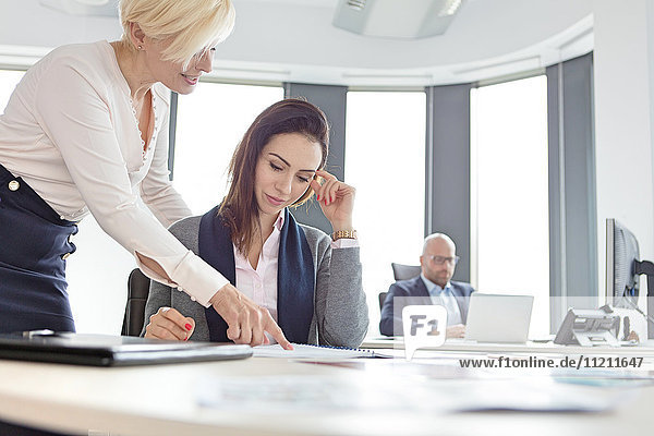 Businesswomen discussing over project with male colleague in background at office