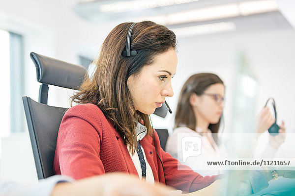 Young businesswoman using headset with female colleague in background at office
