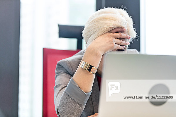 Tired mature businesswoman with head in hands at office