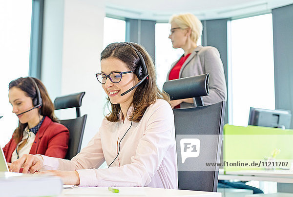 Female customer service representative using headset while colleagues in background at office