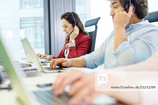 Young businesswoman using headset and laptop with colleagues in foreground at office