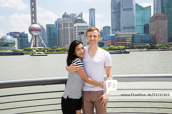 Portrait of smiling couple standing by railing with Shanghai skyline in background