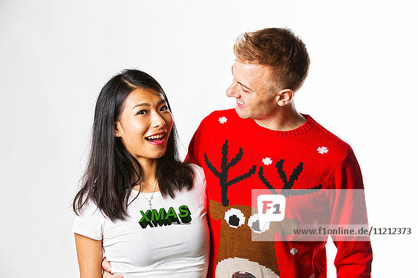 Porträt eines glücklichen multiethnischen Paares in Weihnachtspullis im Studio  das sich gegenseitig anschaut