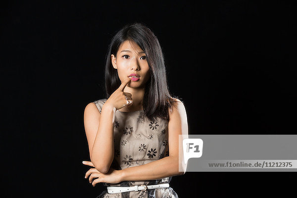 Hübsches chinesisches Mädchen mit Finger auf ihrer Lippe stehend vor schwarzem Hintergrund