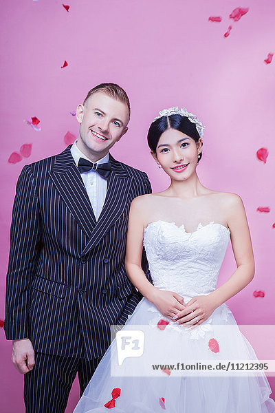 Portrait of happy wedding couple standing against pink background