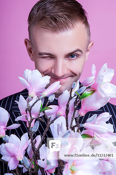 Portrait of bridegroom with artificial flowers winking against pink background
