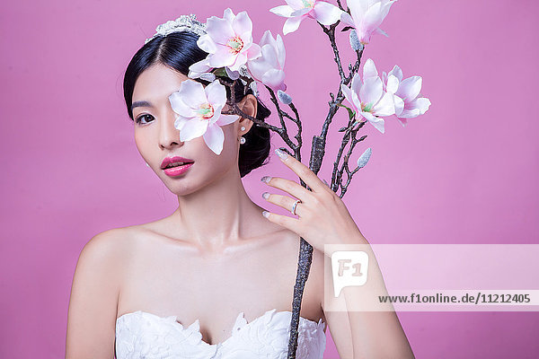 Porträt einer selbstbewussten Braut  die künstliche Blumen vor einem rosa Hintergrund hält