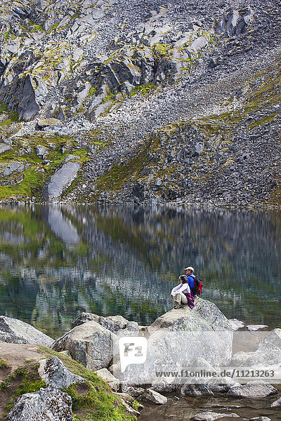 Wanderer sitzen auf einem Felsblock und überblicken den Gold Cord Lake am Hatcher Pass  Süd-Zentral-Alaska  USA