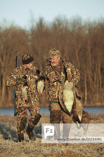 Father And Son Hunters Carrying Decoys And Birds