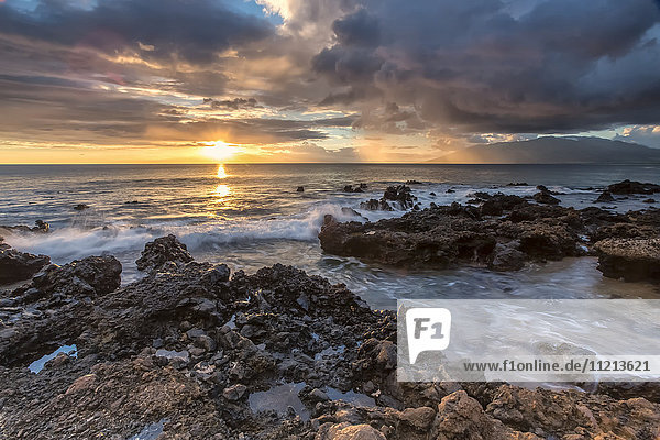 Sonnenuntergang über dem Meer und Wasser  das über die Felsen am Ufer spült; Maui  Hawaii  Vereinigte Staaten von Amerika'.