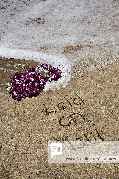 Lei auf dem Sand am Wasser mit der Nachricht 'lei'd on Maui' in den Sand geschrieben; Maui  Hawaii  Vereinigte Staaten von Amerika'.