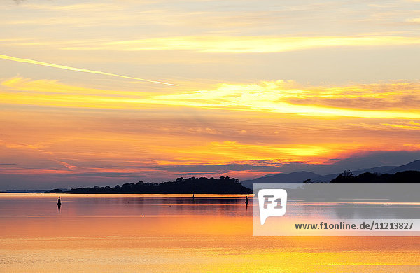 'A dramatic and colourful sunset reflected in water with silhouetted shoreline and mountains; Kenmore County Kerry Ireland'