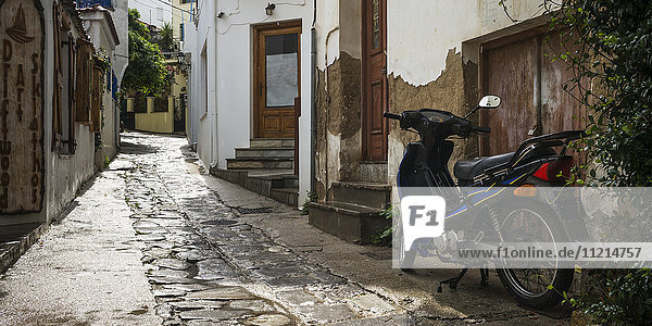 Ein Motorrad  geparkt an einer Hauswand in einer abgenutzten Kopfsteinpflaster-Gasse; Skiathos  Griechenland