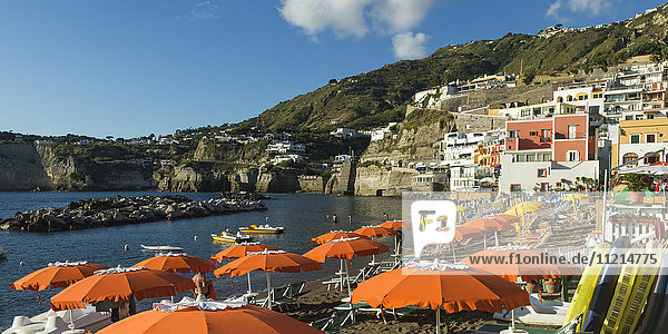 Bunte Gebäude und orangefarbene Sonnenschirme am Strand einer Ferienanlage an der Küste der Insel Ischia; Ischia  Kampanien  Italien'.