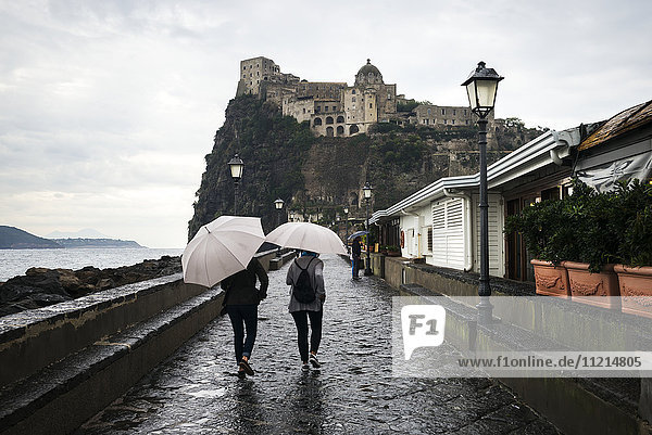 Fußgänger  die an einem regnerischen Tag mit Regenschirmen in Richtung der Burg Aragonese gehen; Ischia  Kampanien  Italien'.