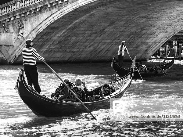 'Gondoliers paddling a gondola with passengers in a canal; Venice  Italy'