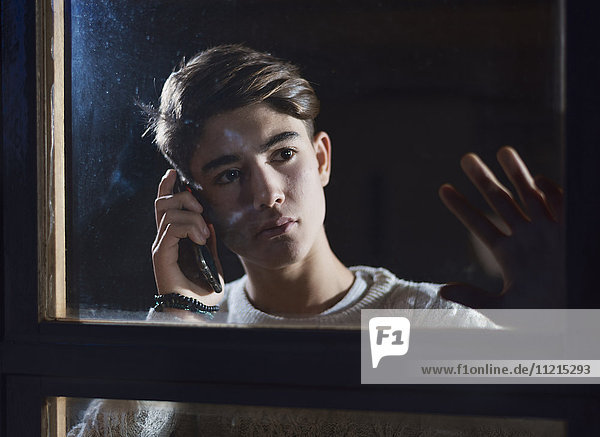 Ein junger Mann telefoniert mit seinem Handy  während er aus dem Fenster schaut; Tarifa  Cadiz  Andalusien  Spanien'.