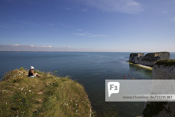Frau sitzt auf einer Klippe bei Old Harry's Rocks  Isle of Purbeck