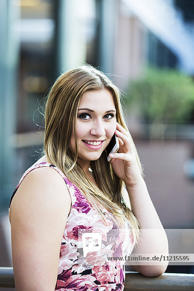 Eine hübsche junge Geschäftsfrau der Jahrtausendwende  die in der Lobby eines Bürogebäudes mit ihrem Smartphone telefoniert; Edmonton  Alberta  Kanada'.