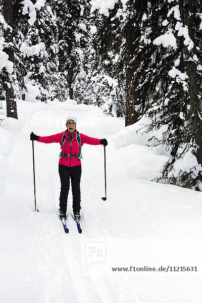 'Female cross country skier on groomed trail with arms out to the side going downhill and excited expression; Lake Louise  Alberta  Canada'