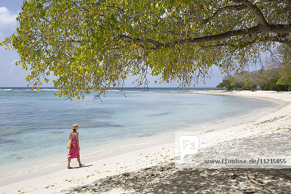 Frau im Bikini spaziert am Ufer eines weißen Sandstrandes