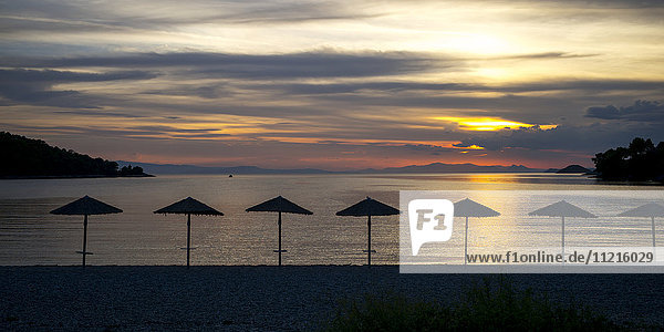Silhouette von Sonnenschirmen am Strand bei Sonnenuntergang auf einer griechischen Insel im Ägäischen Meer; Panormos  Thessalia Sterea Ellada  Griechenland'.